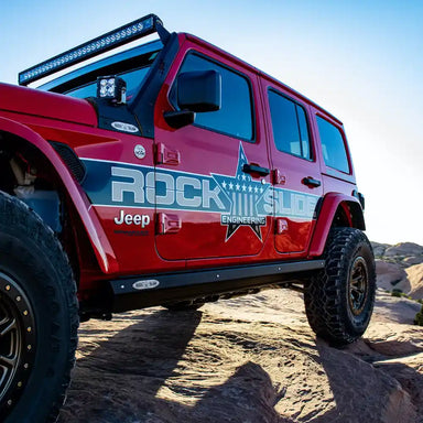 Red Jeep Wrangler JL Rubicon with Rock Slide step sliders and large tires on rocky terrain