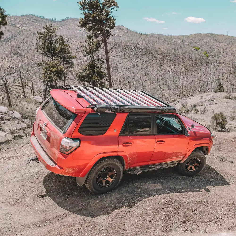 Red SUV with a roof rack and mounted Southern Style rock sliders on a mountainous terrain