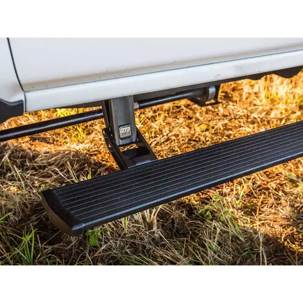 Retractable AMP PowerStep extended under a Chevrolet Silverado on off-road terrain.