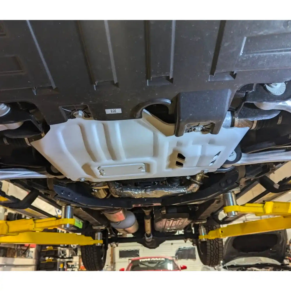 Close-up of a vehicle's undercarriage skid plate with suspension components on a lift.