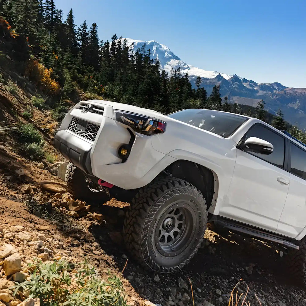 White off-road vehicle with souther style rock sliders on a mountain trail with snow-capped mountains in the background
