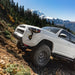 White off-road vehicle with souther style rock sliders on a mountain trail with snow-capped mountains in the background