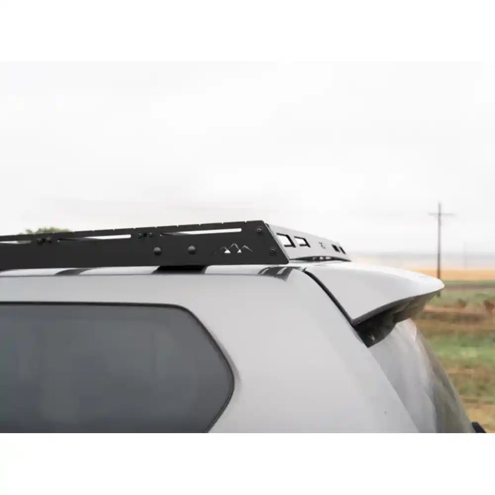 Side detail of black RCI rack crossbars and side rails secured to GX460 roof under cloudy sky