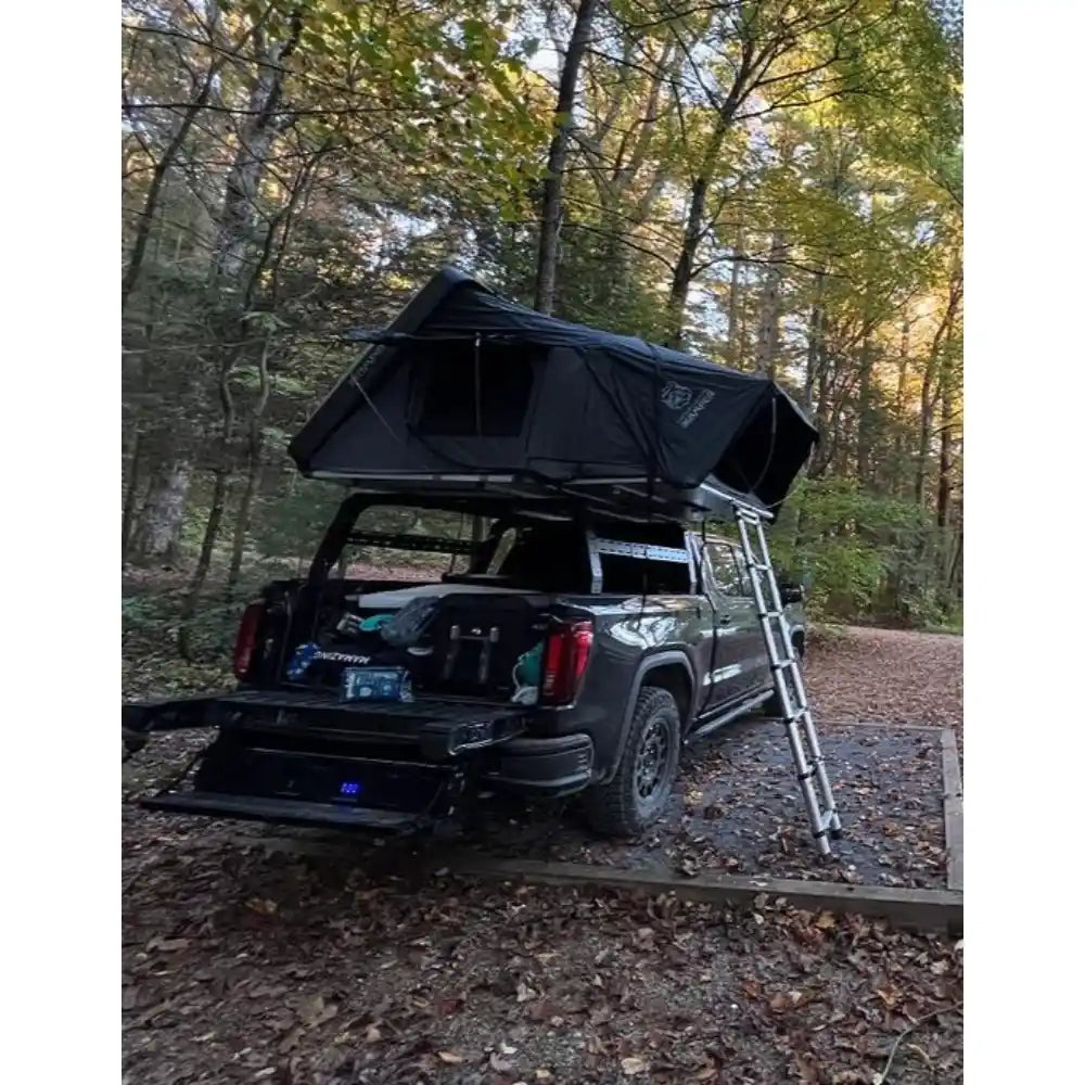 Black truck with a rooftop tent parked in a forest