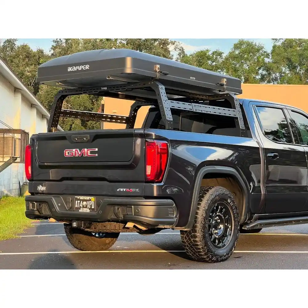 Black GMC truck with a Bed rack and 'iKamper' brand canopy in an outdoor setting.