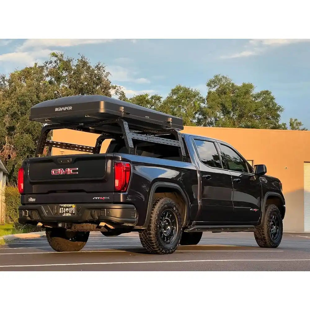 Black GMC truck with a rooftop storage box on a bed rack in an outdoor setting