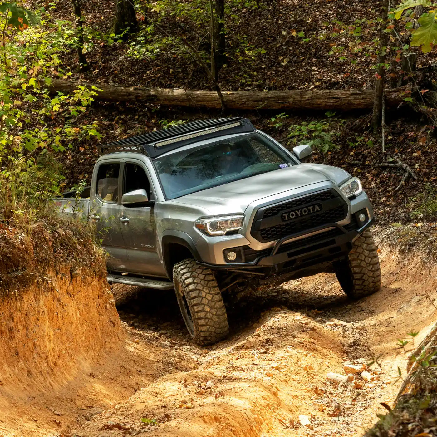 Silver Toyota truck driving on a dirt trail in a forest with southern style offroad rock sliders