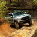 Silver Toyota truck driving on a dirt trail in a forest with southern style offroad rock sliders
