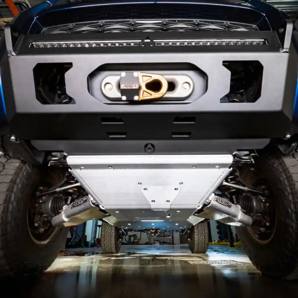 Close-up of a vehicle's bumper and front and lower a-arm skid plates in a workshop setting.