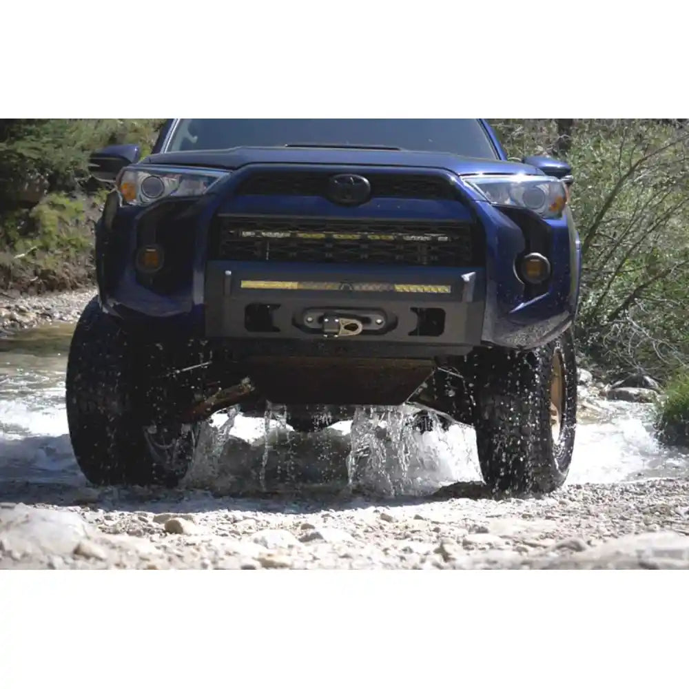 Blue Toyota 4Runner driving through water on a dirt road with trees in the background