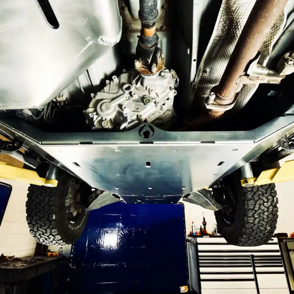 Undercarriage of a 4runer with mounted skid plate and mechanical components visible in a workshop setting.