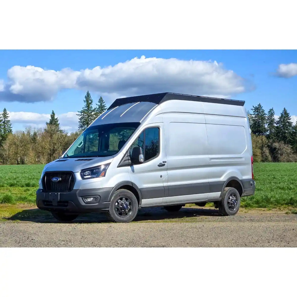 White Tranist with a black stealth+ roof rack on a gravel road with trees and blue sky in the background