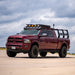 Maroon pickup truck with bed rack and additional equipment on a road with a cloudy sky.