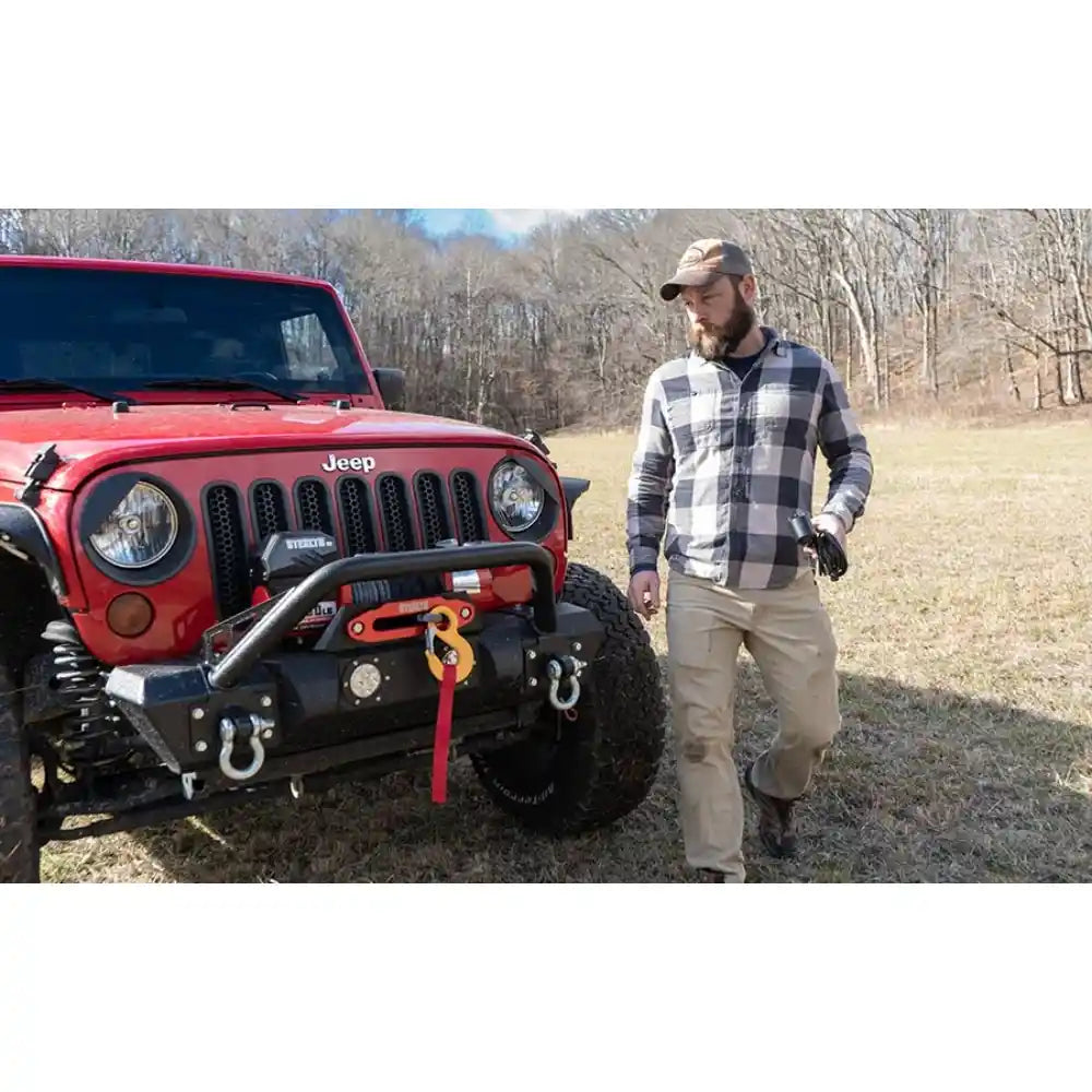 Man standing next to a red Jeep with winch mounted in an outdoor setting with trees in the background