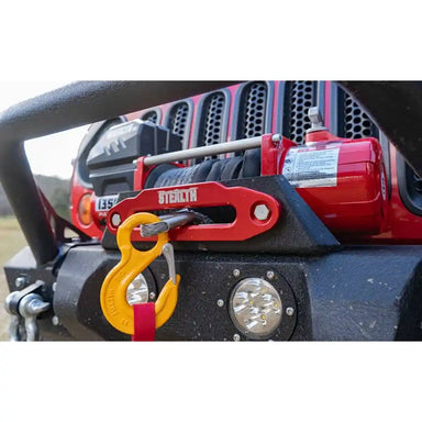Red Warrior Stealth winch on a vehicle with a yellow hook, set against a blurred background.