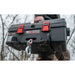 Person carrying a large gray Trojan 12v Portable Utility Winch with red latches on a blurred outdoor background
