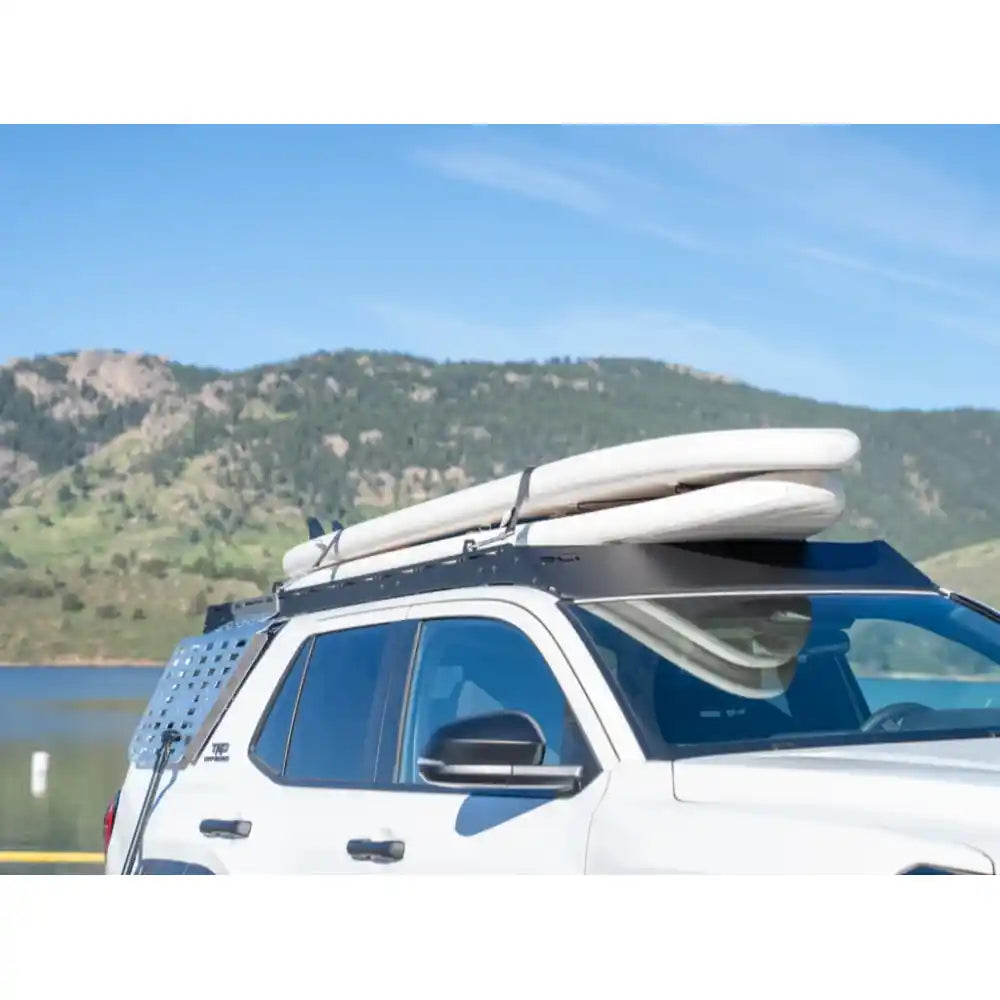 White 4Runner at lake edge with RCI rack loaded, red shelters and calm water backdrop