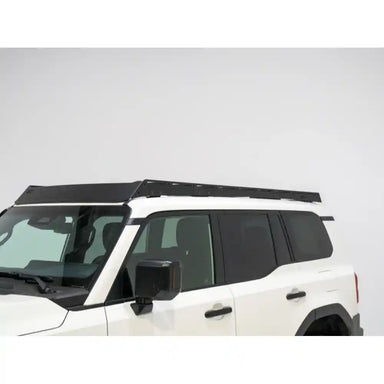 White Land Cruiser 2024+ parked in bright indoor space with sleek black RCI full-length roof rack installed