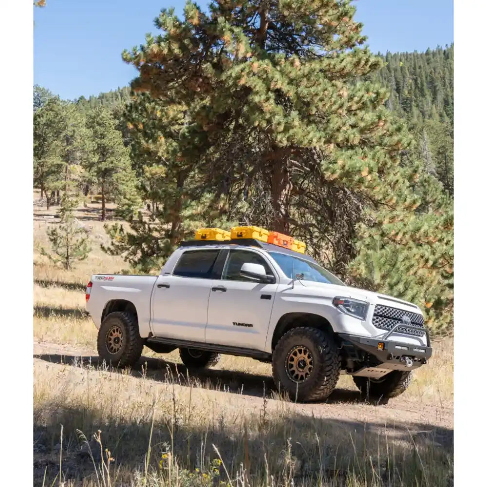 White Toyota Tundra climbing rugged terrain, black RCI roof rack loaded and stable
