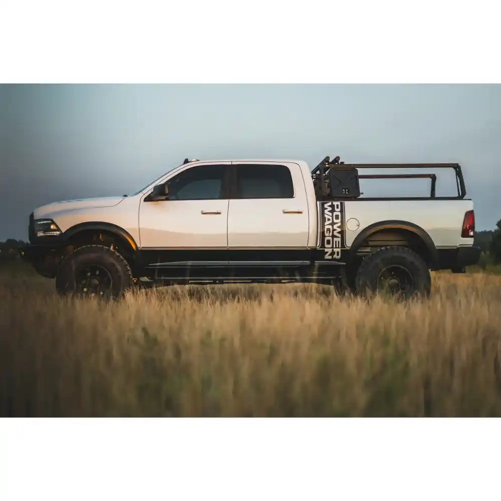 White pickup RAM with installed bed rack and with large tires in a field