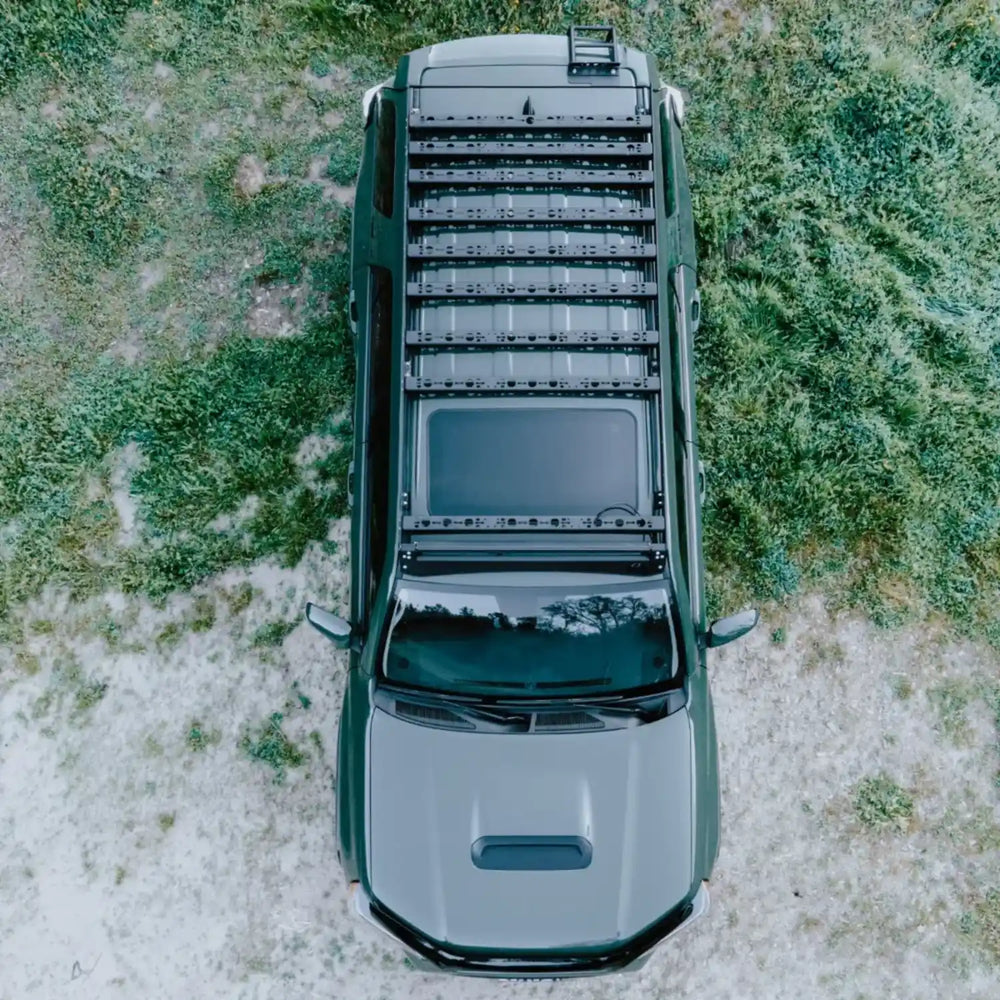 Top-down view of a green SUV with an all prop 4runner roof rack on a grassy field.