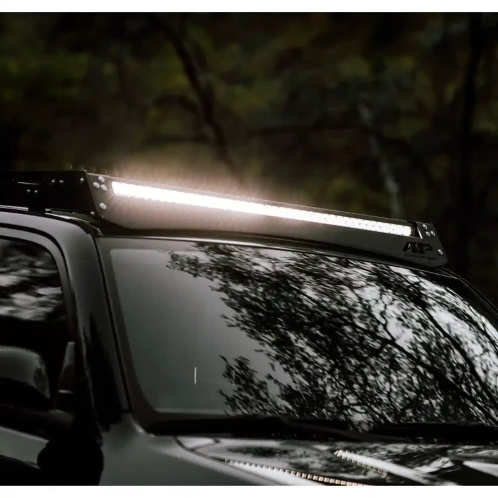Car roof with a mounted LED light bar om roof rack in a dark forest setting