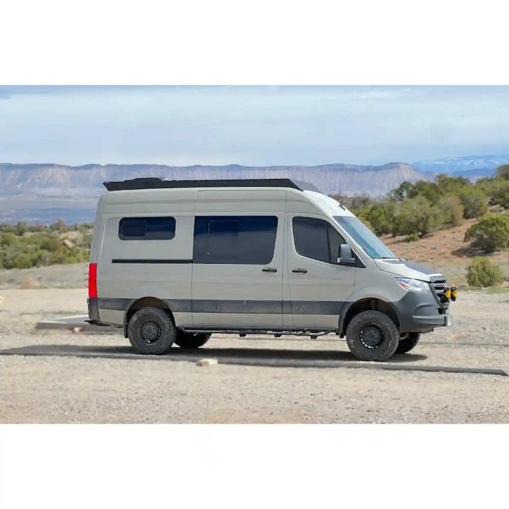 Side view of the sprinter with installed roof rack parked on a dirt road with mountains in the background