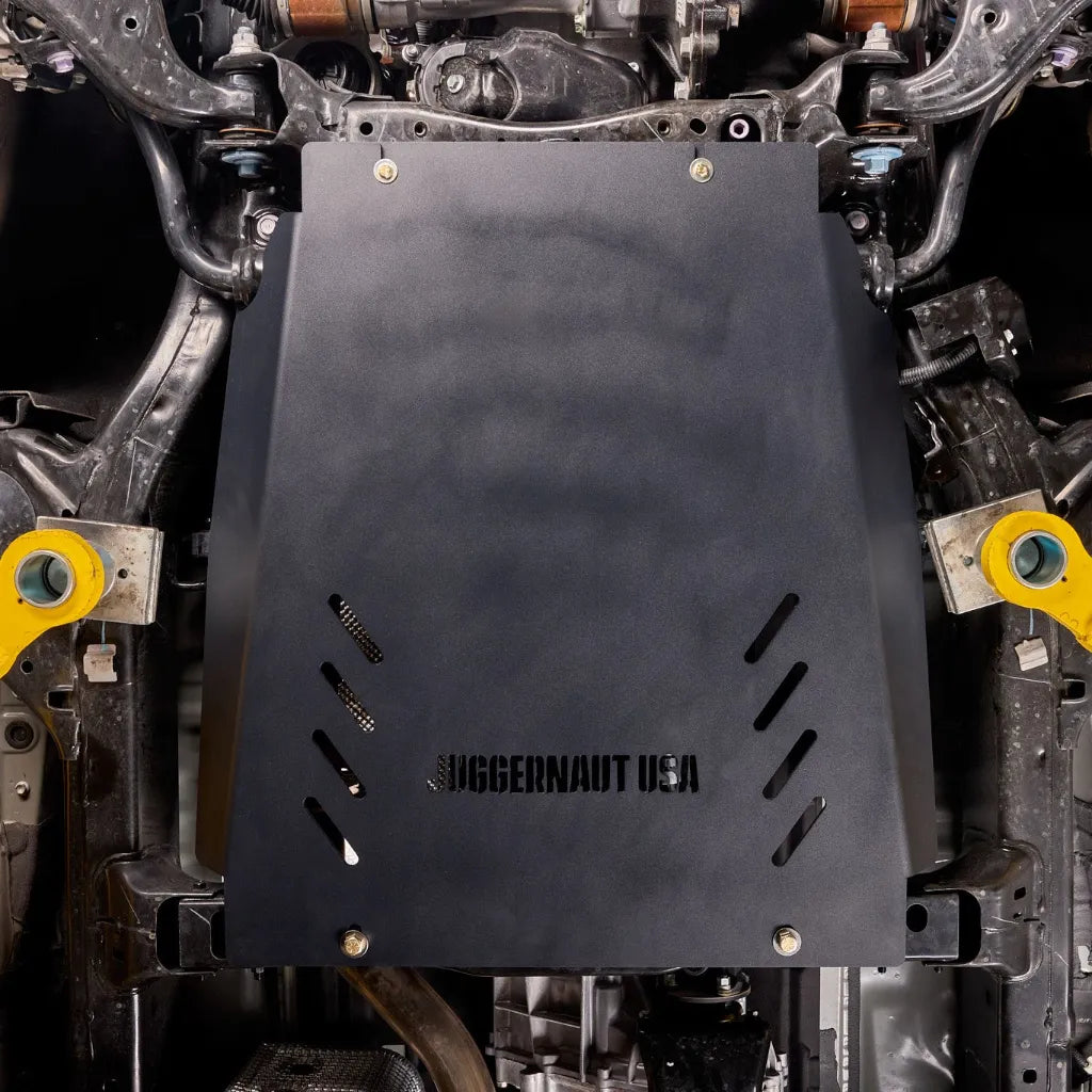 Front three-quarter underbody view of the transmission skid plate installed between the 4Runner's front suspension arms, showing mounting bolts