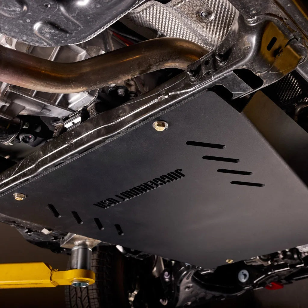 Rear-angle underbody view of the transmission skid plate installed alongside the exhaust pipe