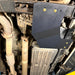Close-up of the Juggernaut transfer case skid plate mounted near the crossmember of a 2009-2014 Ford F-150