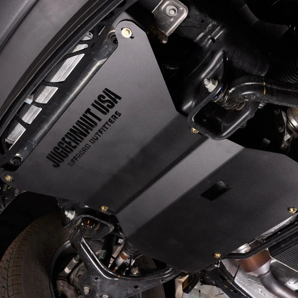 Angled underbody view of the Ford F-150 engine skid plate installed near the front wheel well and suspension