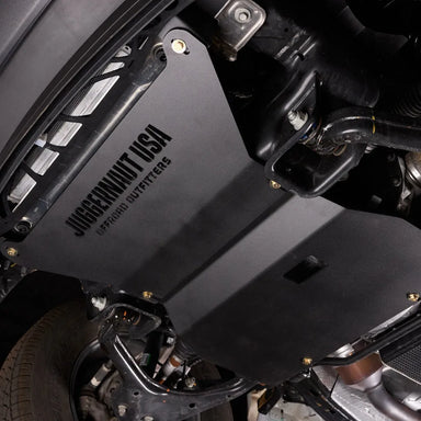 Angled underbody view of the Ford F-150 engine skid plate installed near the front wheel well and suspension