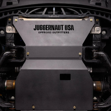 Juggernaut Ford F-150 engine skid plate installed, straight-on underbody view showing the embossed JUGGERNAUT USA logo behind the front bumper