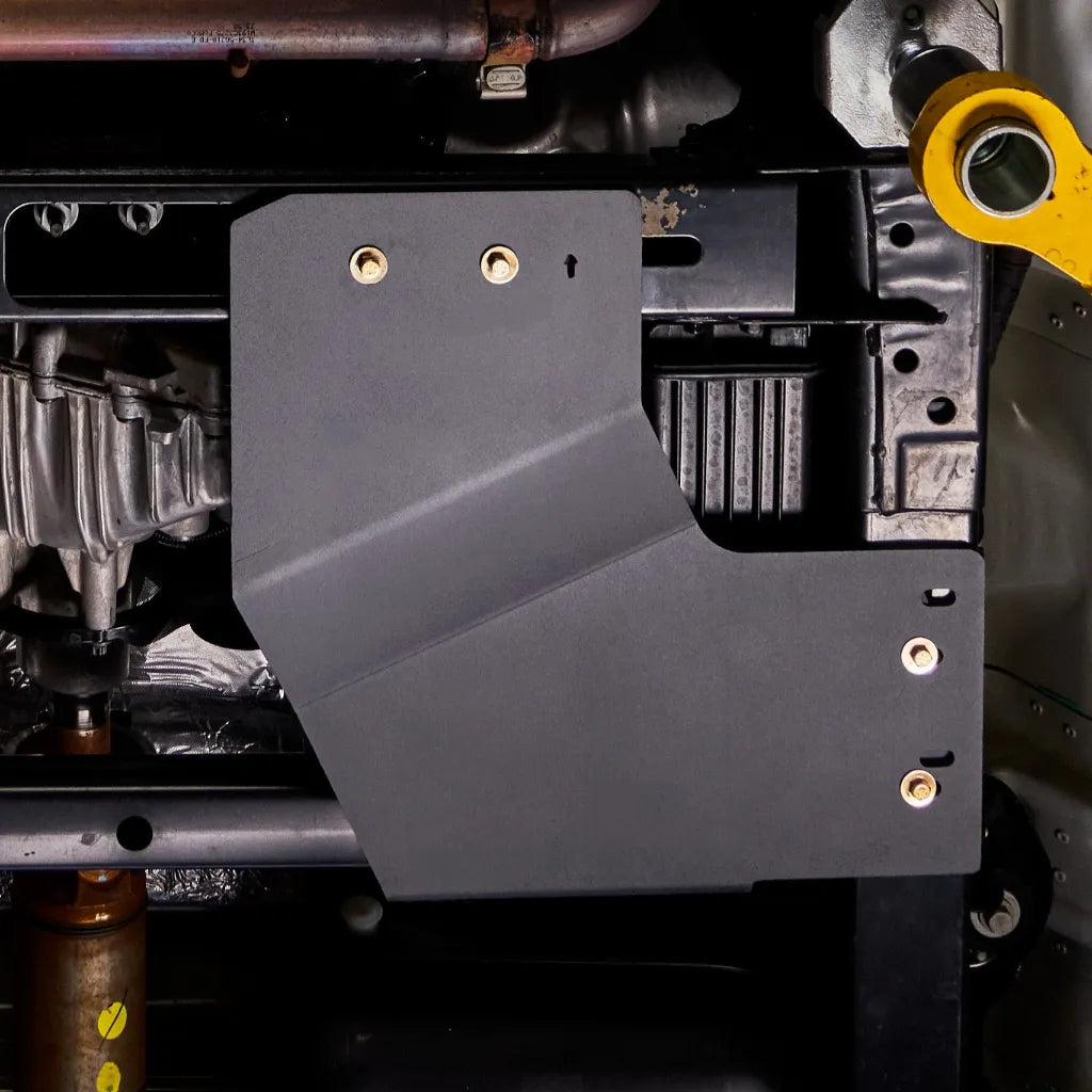 Close-up underbody view of the Ford F-150 transfer case skid plate installed near the driveshaft, mounted with visible bolts