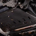 Close-up underbody view of the transmission skid plate installed near the catalytic converter and exhaust, mounted with visible bolts