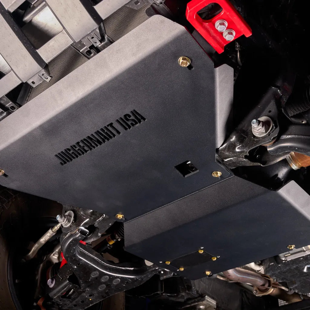 Front-angle underbody view of the engine skid plate installed near the front suspension