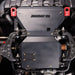 Straight-on underbody view of the engine skid plate installed, showing the JUGGERNAUT USA logo and red-capped mounting hardware