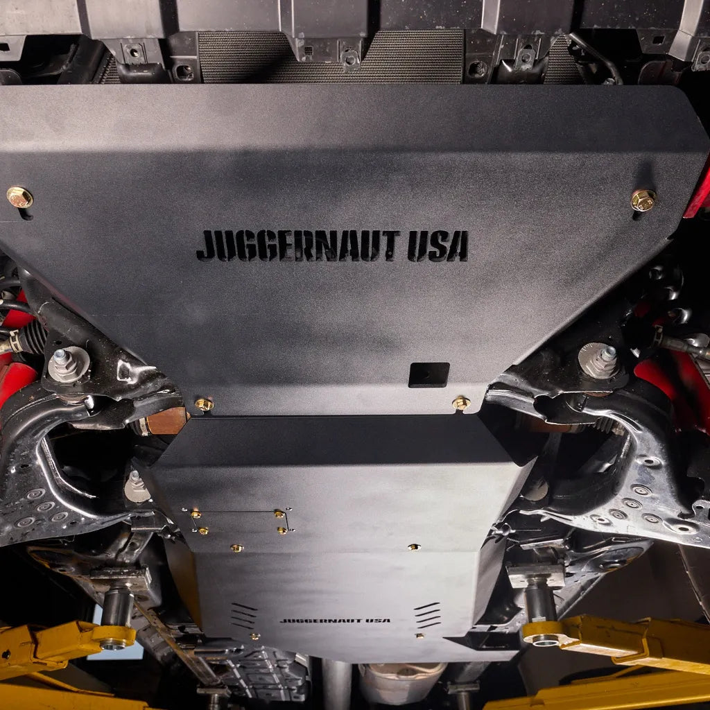 Close-up underbody view of the engine skid plate section of the package installed, showing the JUGGERNAUT USA logo