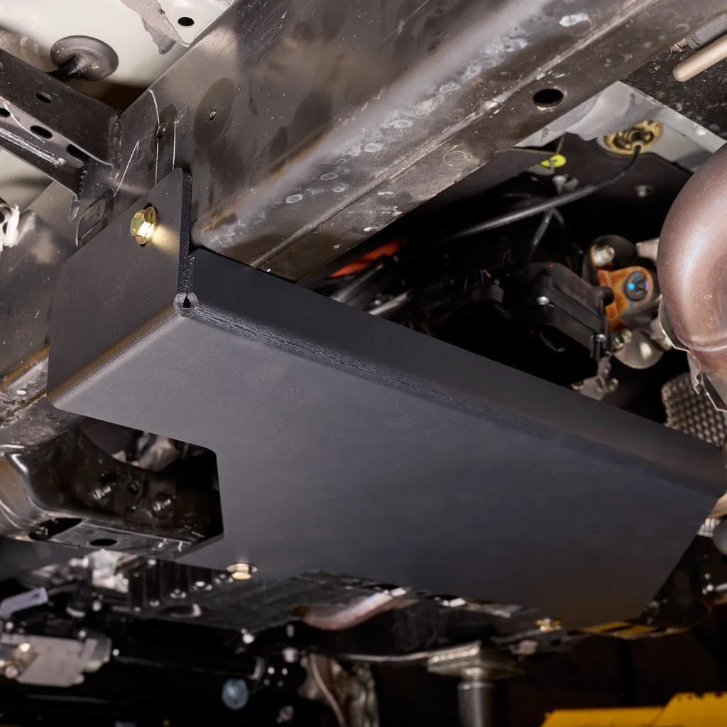 Underbody angle view of the transfer case skid plate mounted along the frame rail near the driveshaft