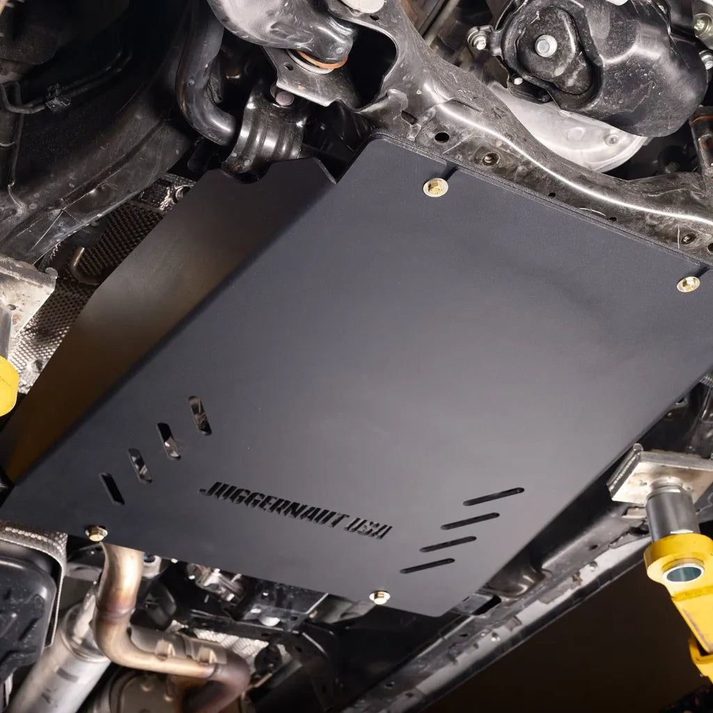 Angled underbody view of the transmission skid plate mounted near the exhaust pipe
