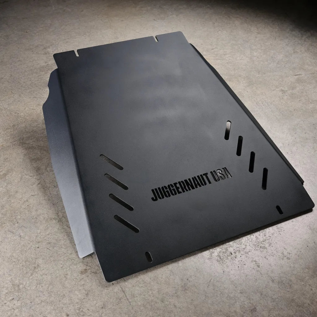Juggernaut Tacoma transmission skid plate, standalone product view on shop floor showing the embossed JUGGERNAUT USA logo and slotted vent cutouts