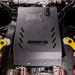 Juggernaut USA transmission skid plate and catalytic converter shield installed on a Chevy Silverado 1500, straight-on underbody view showing the removable oil-drain access panel and mounting bolts