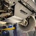 Front-quarter view of the engine skid plate installed on a shop lift, with the driver-side wheel and tire visible