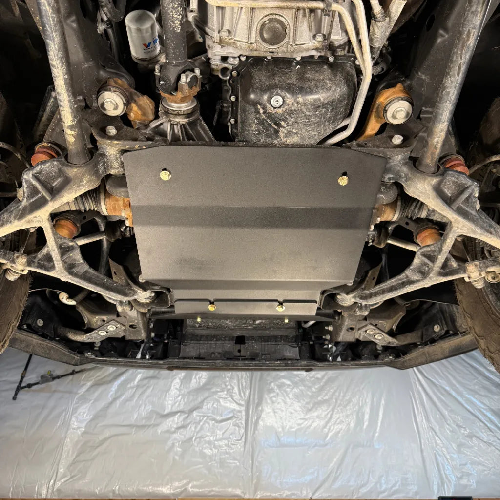 Close-up angled view of the engine skid plate from above and behind, showing the oil filter and control arms it clears