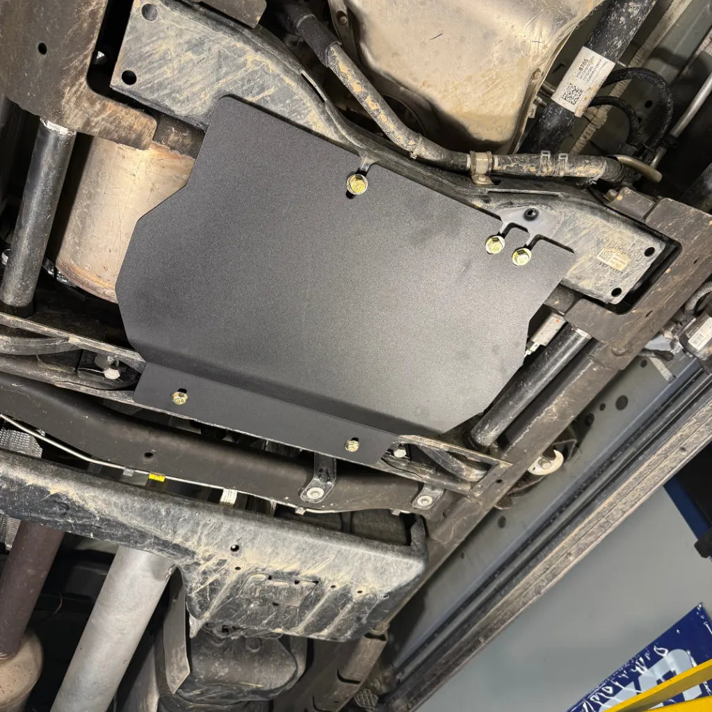 Close-up angled view of the transfer case skid plate installed near the exhaust and driveline, showing mounting bolts
