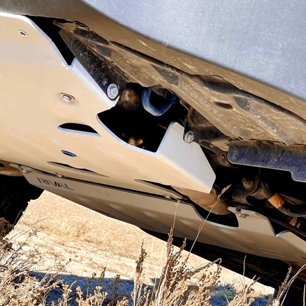 Close-up of a vehicle's undercarriage with a white skid plate, on a rocky terrain.