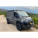 Promaster with installed roof rack front lights on a dirt road with a scenic background