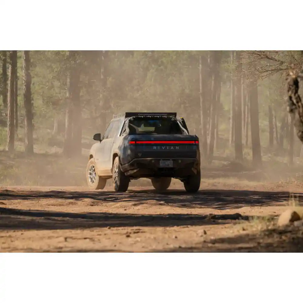 Rivian R1T with Rago chase rack on dusty trail, rear view
