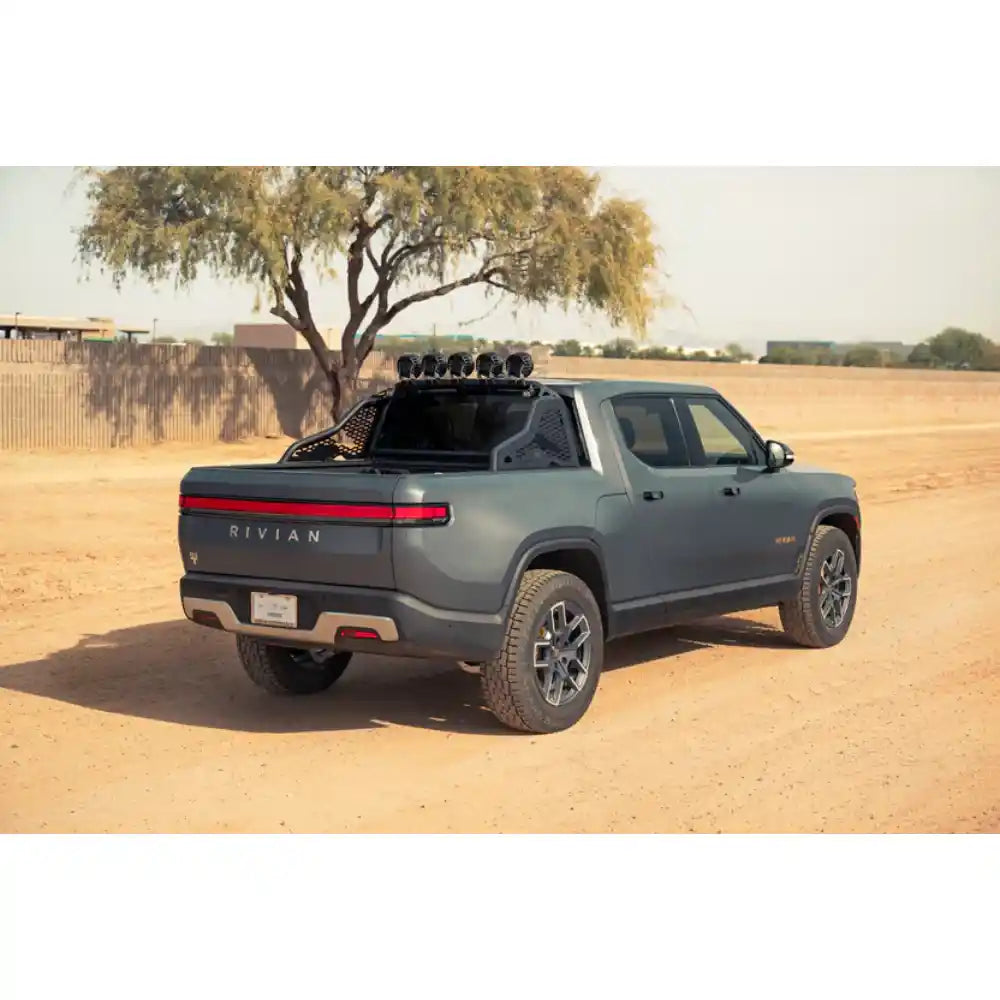 Rivian R1T with Rago chase rack among trees, rear three-quarter
