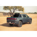 Rivian R1T with Rago chase rack among trees, rear three-quarter